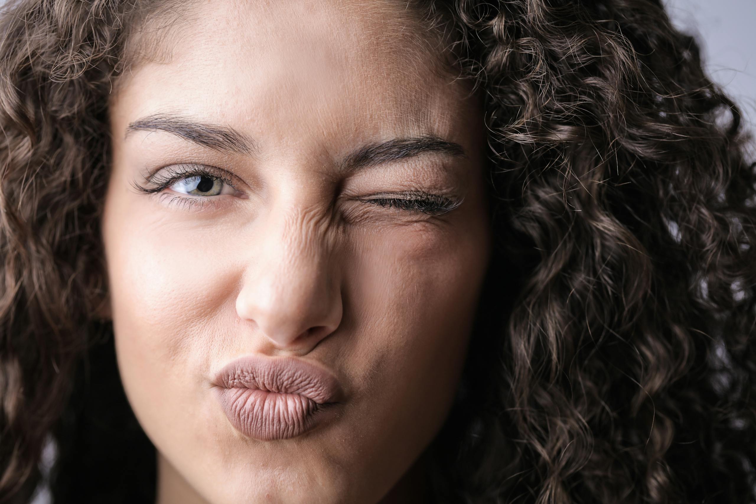 A playful close-up portrait of a woman with curly hair and a winking eye, expressing fun and mischief.
