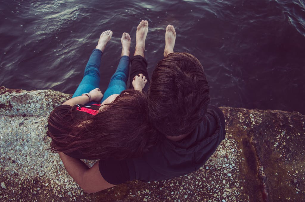 A romantic couple sitting on a rocky pier, enjoying a serene moment by the water.