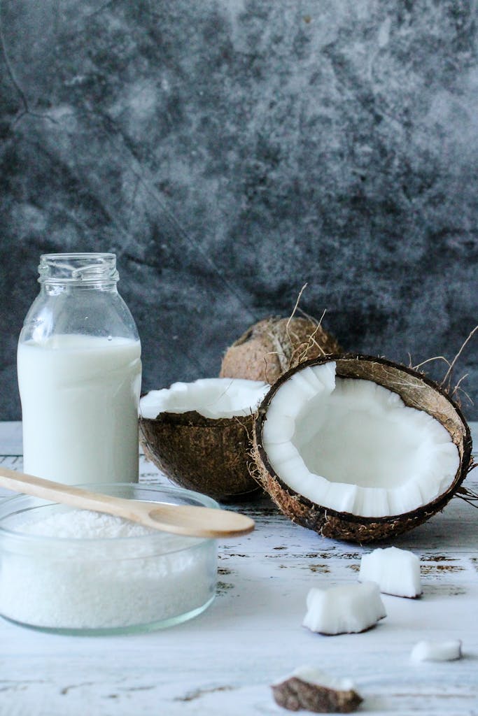 A rustic composition of fresh coconut milk, shredded coconut, and coconut shells on a table.