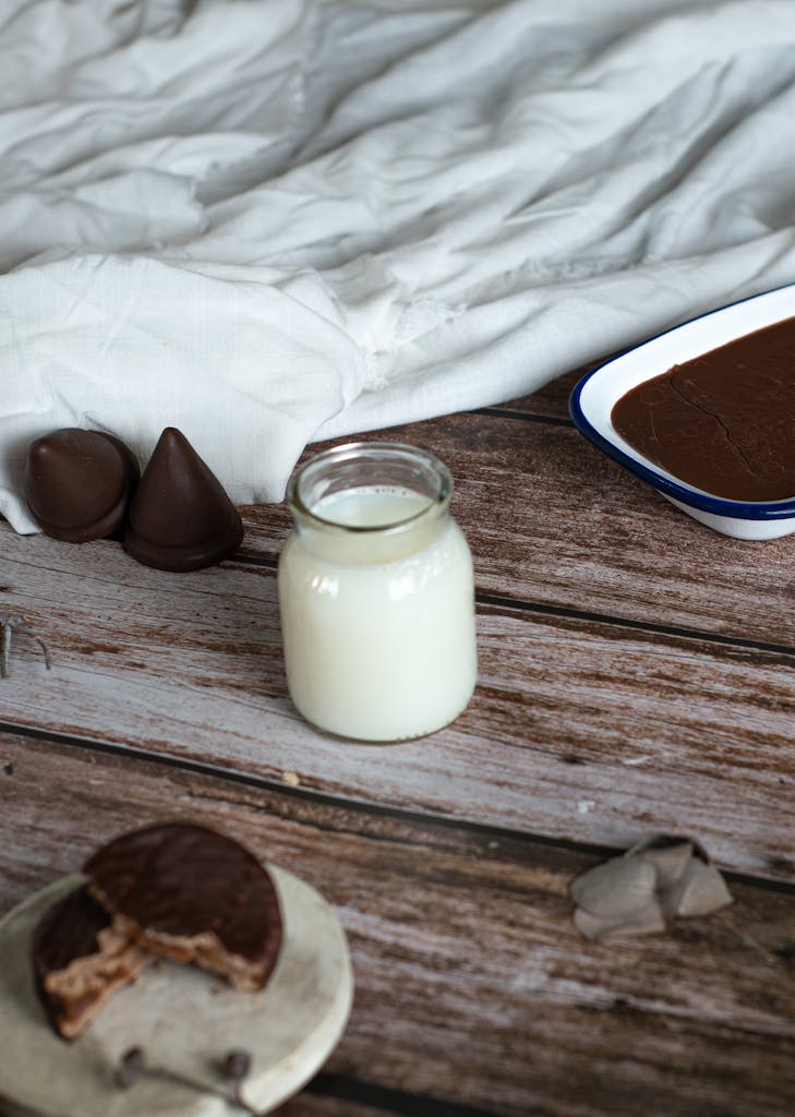A rustic setting featuring a jar of milk and assorted chocolate desserts on a wooden surface.