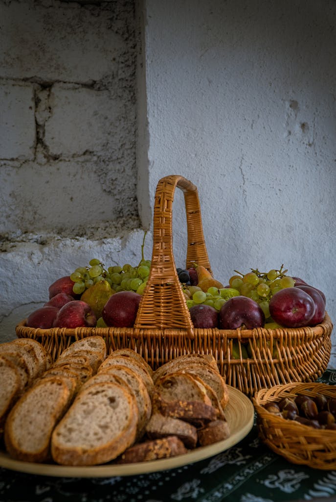A rustic setting with fresh bread loaves and a wicker basket filled with grapes and plums.