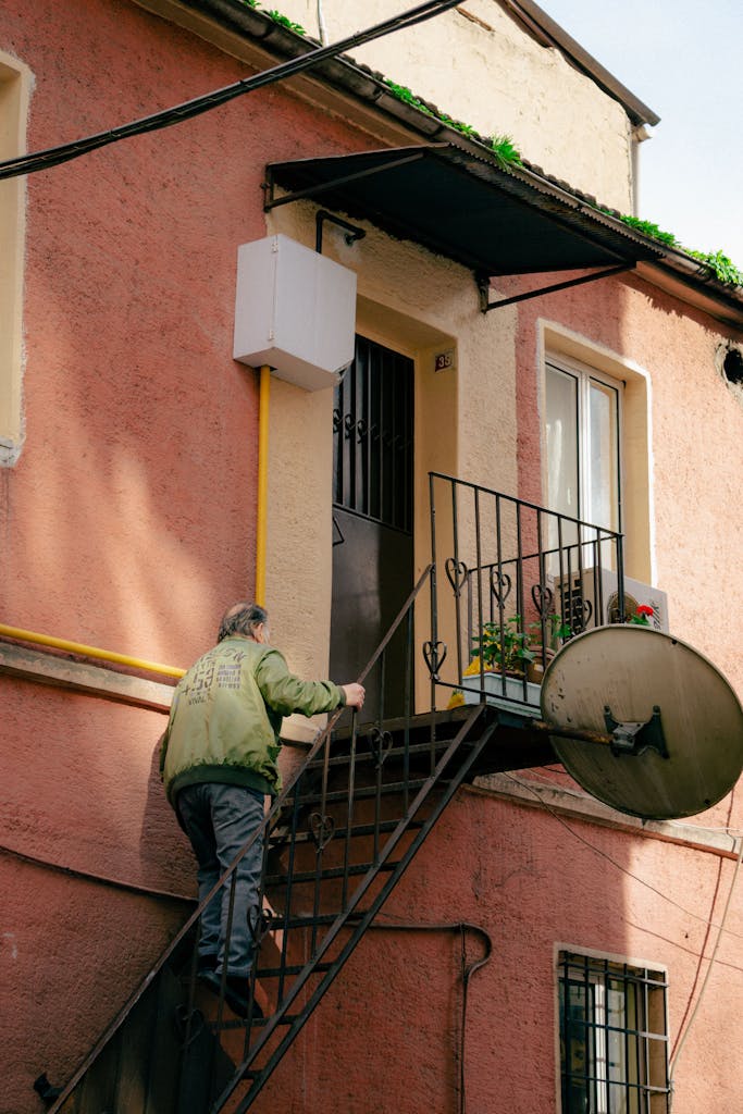 A senior man climbs exterior stairs to a residential urban home, emphasizing independent living.