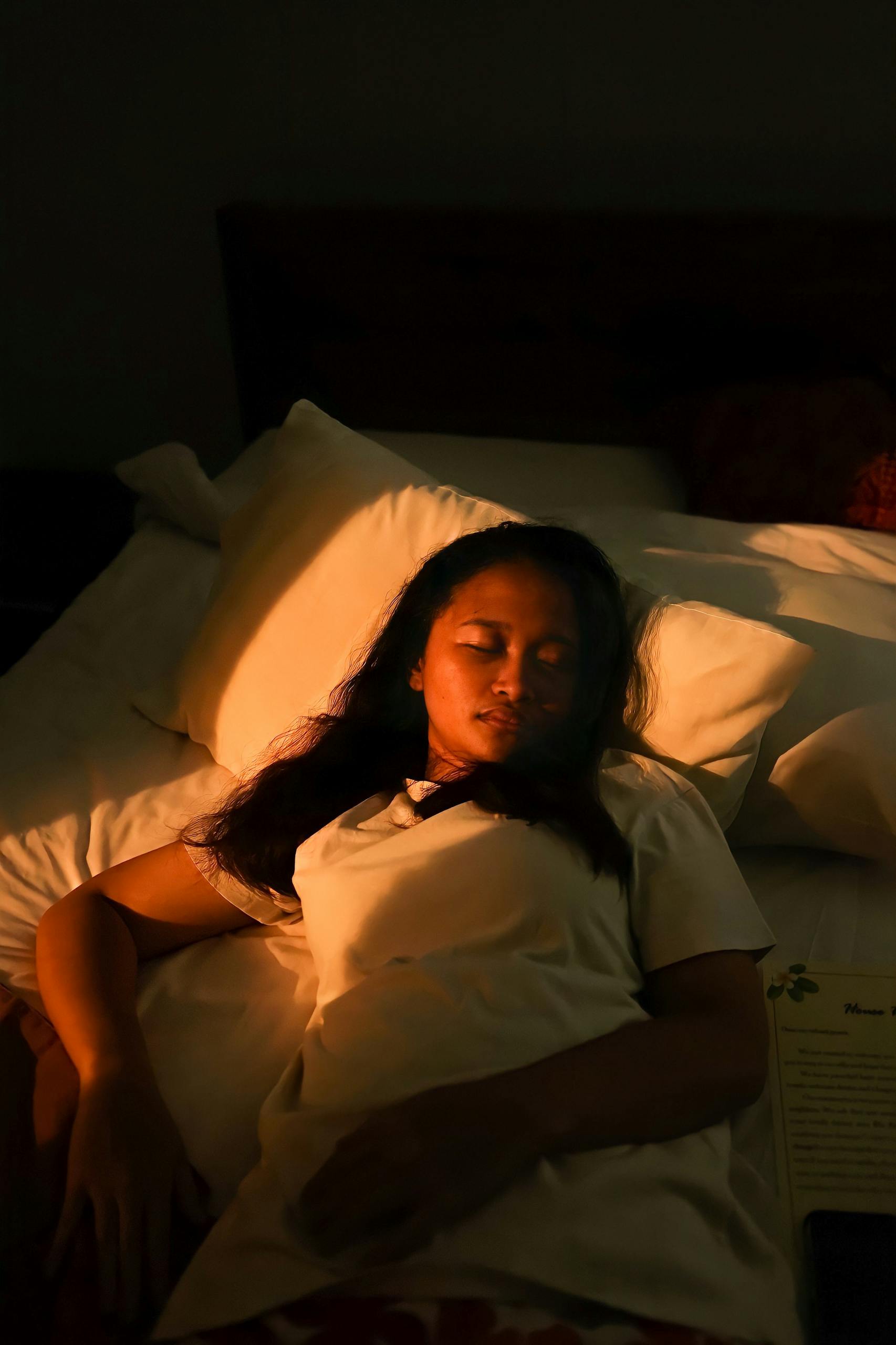 A serene woman sleeping on a bed, bathed in warm evening light.
