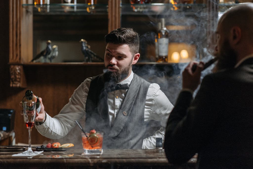 A stylish bartender prepares cocktails in a smoky, elegant bar setting.