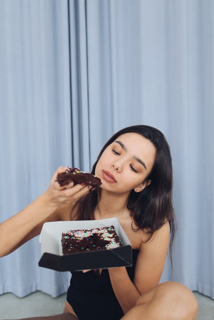 A woman enjoys a delicious chocolate cake indoors, savoring the sweet treat.
