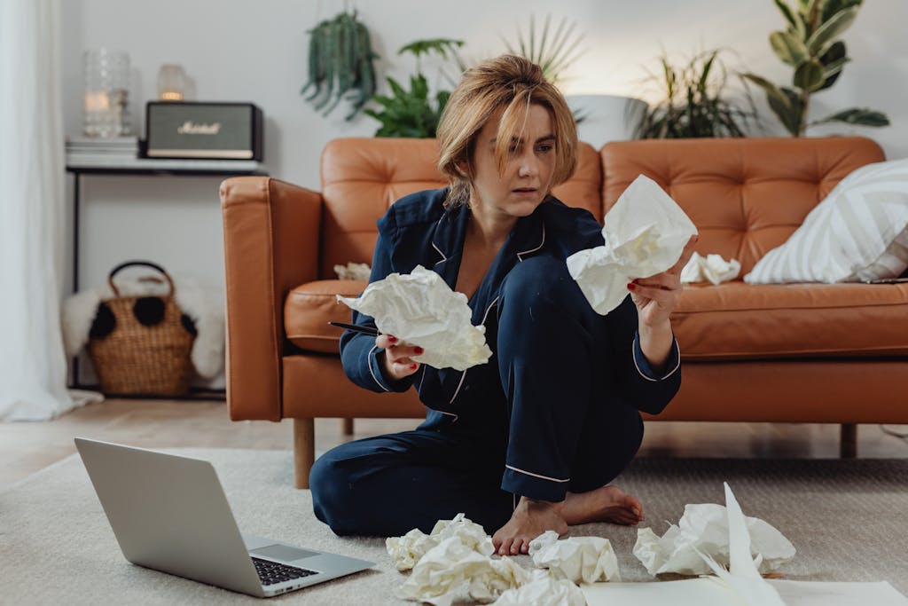 A woman in comfortable loungewear surrounded by crumpled papers, working remotely from home.