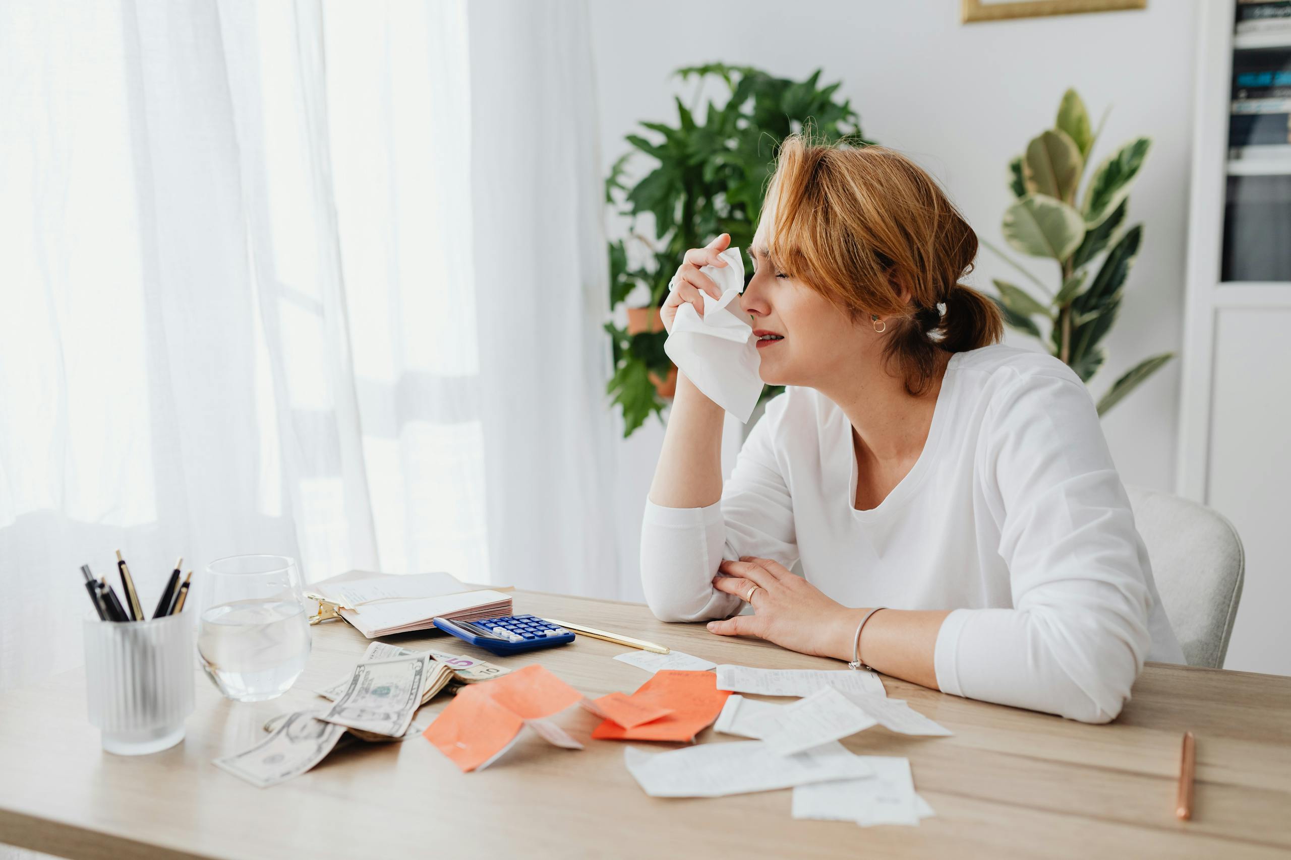 A woman is overwhelmed by bills and finances, sitting at a desk indoors.