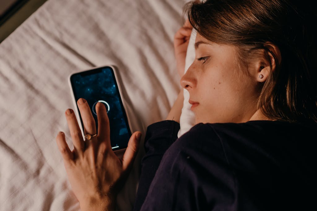 A woman lying in bed, engaged with her smartphone, creating a tranquil nighttime scene.