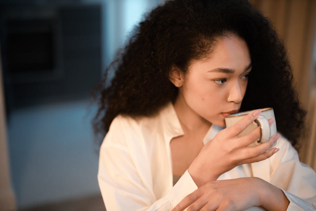 A woman with curly hair savoring a cup of coffee indoors, embracing a peaceful morning atmosphere.