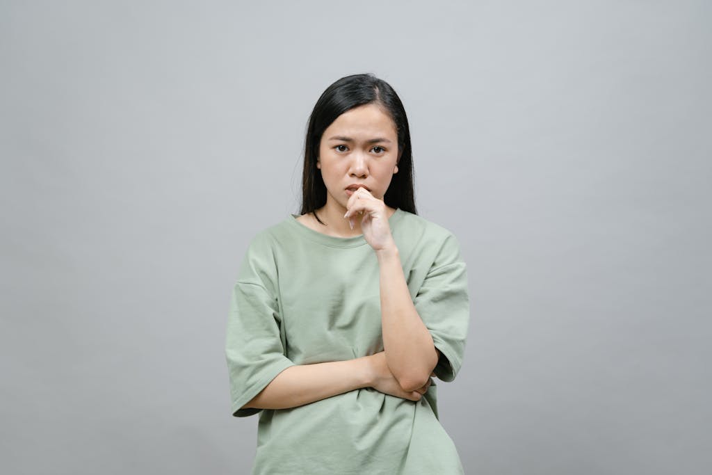 A young Asian woman appears thoughtful and introspective against a gray studio background.