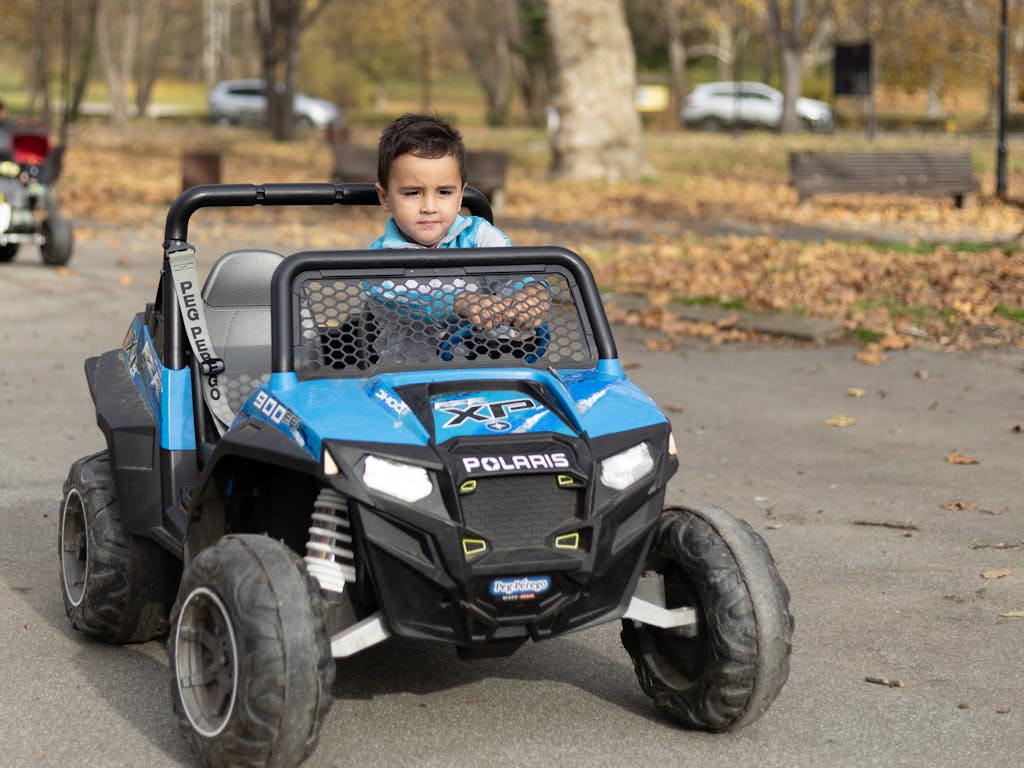 A young boy riding a blue electric toy quad bike on a sunny day in the park.