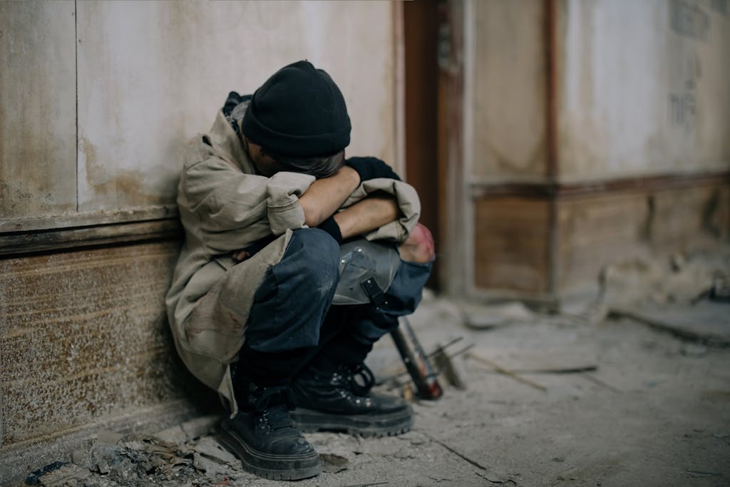 A young boy sits alone, appearing sad and forlorn, in an abandoned building setting.
