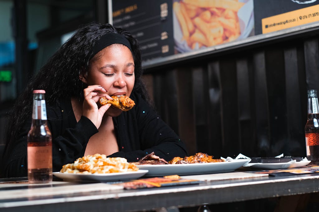 A young woman enjoying a chicken meal at a restaurant, accompanied by drinks and fries.