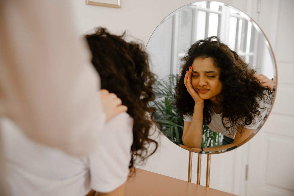 A young woman in front of a mirror expressing self-doubt and contemplation indoors.