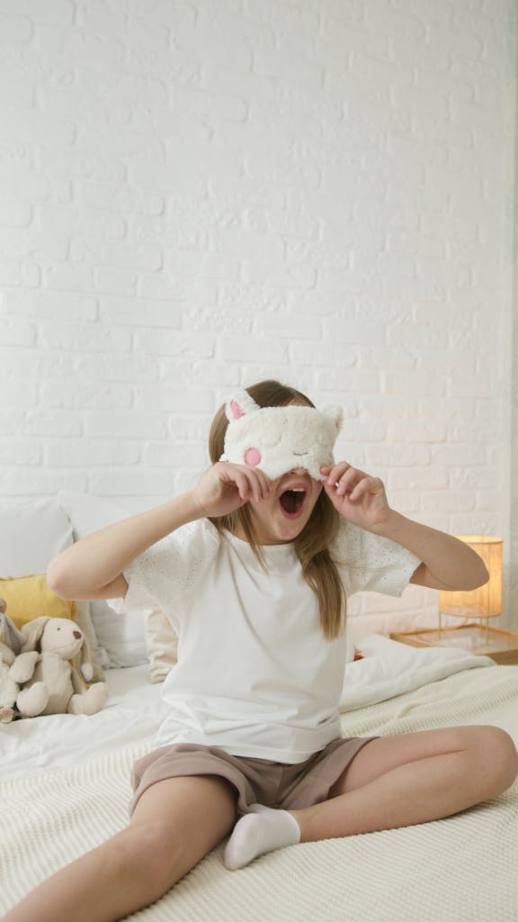 Adorable girl with eye mask yawning on bed, embodying childhood innocence and sleepiness.