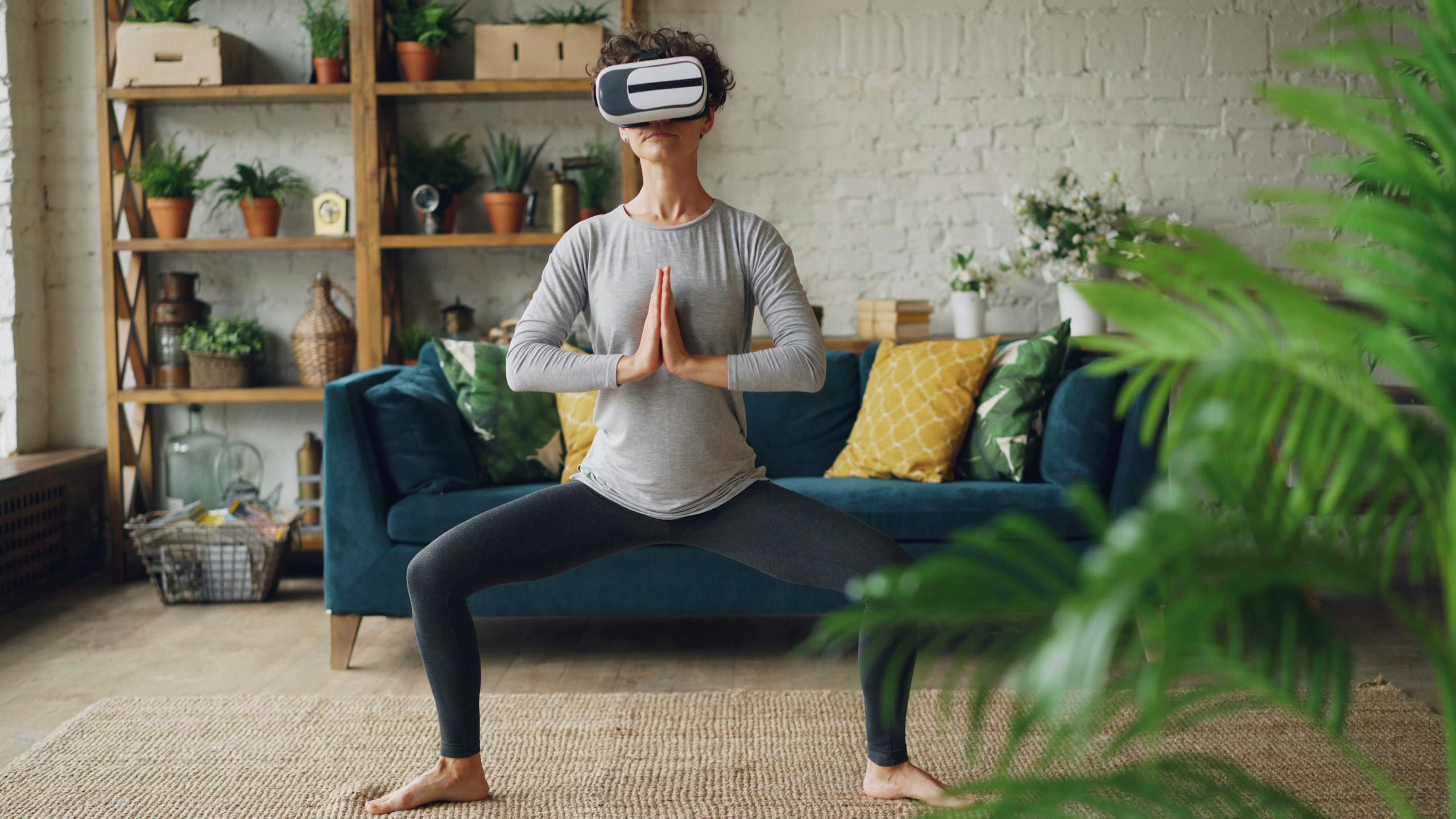 Adult woman using a VR headset while practicing yoga indoors in a modern living room setting.