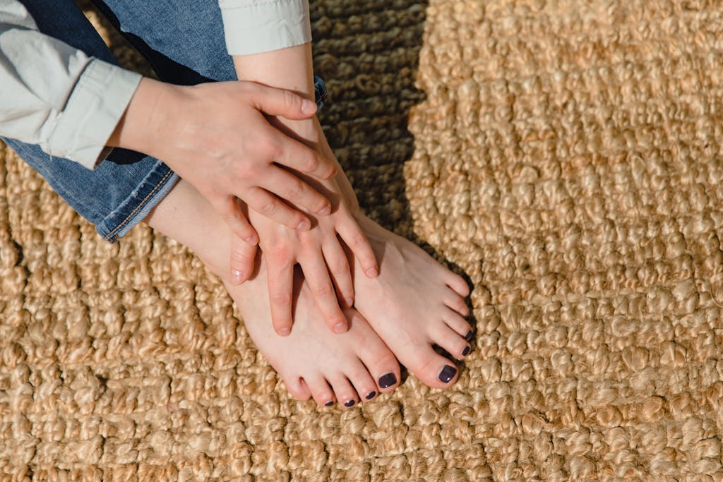 Adult woman with manicured nails relaxes barefoot on a woven rug, enjoying a moment of tranquility indoors.