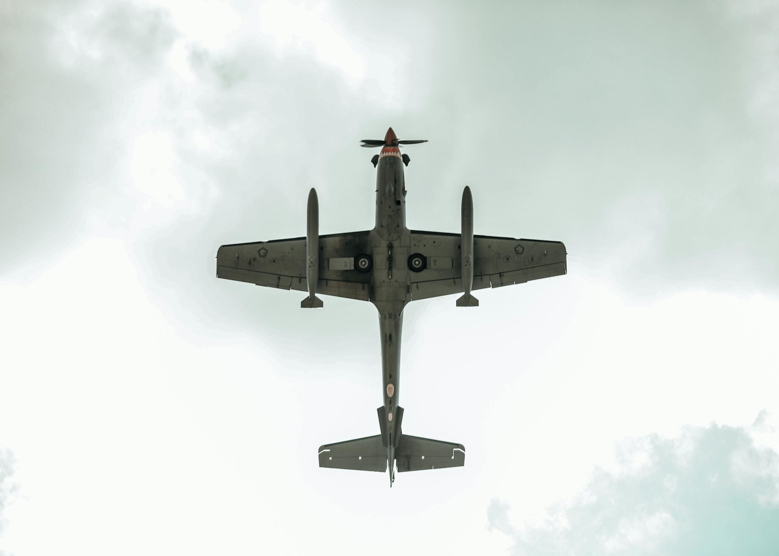 Aerial perspective of a plane flying overhead with clouds in the background.
