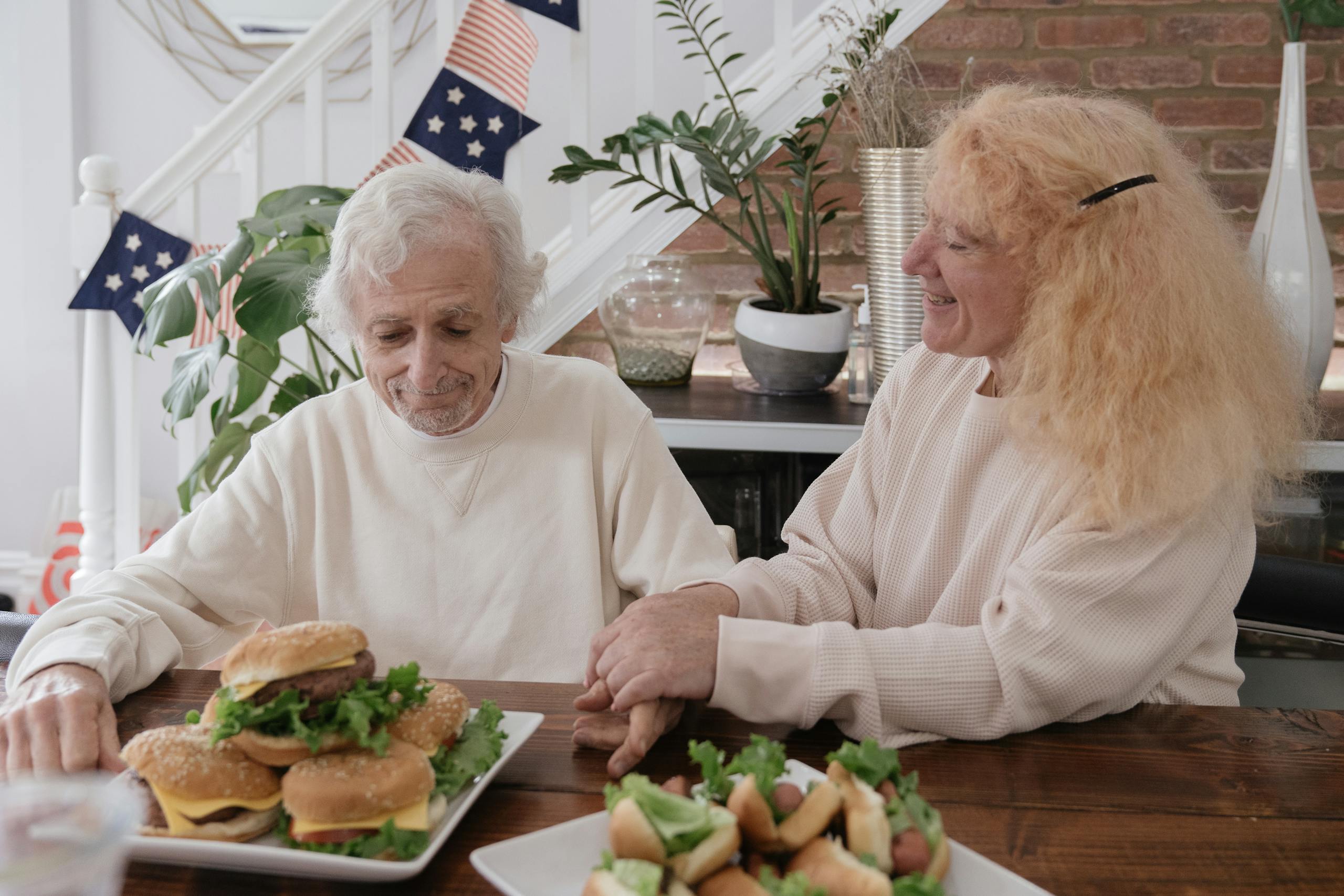An elderly couple shares a meal and moments together at home, enjoying hamburgers.