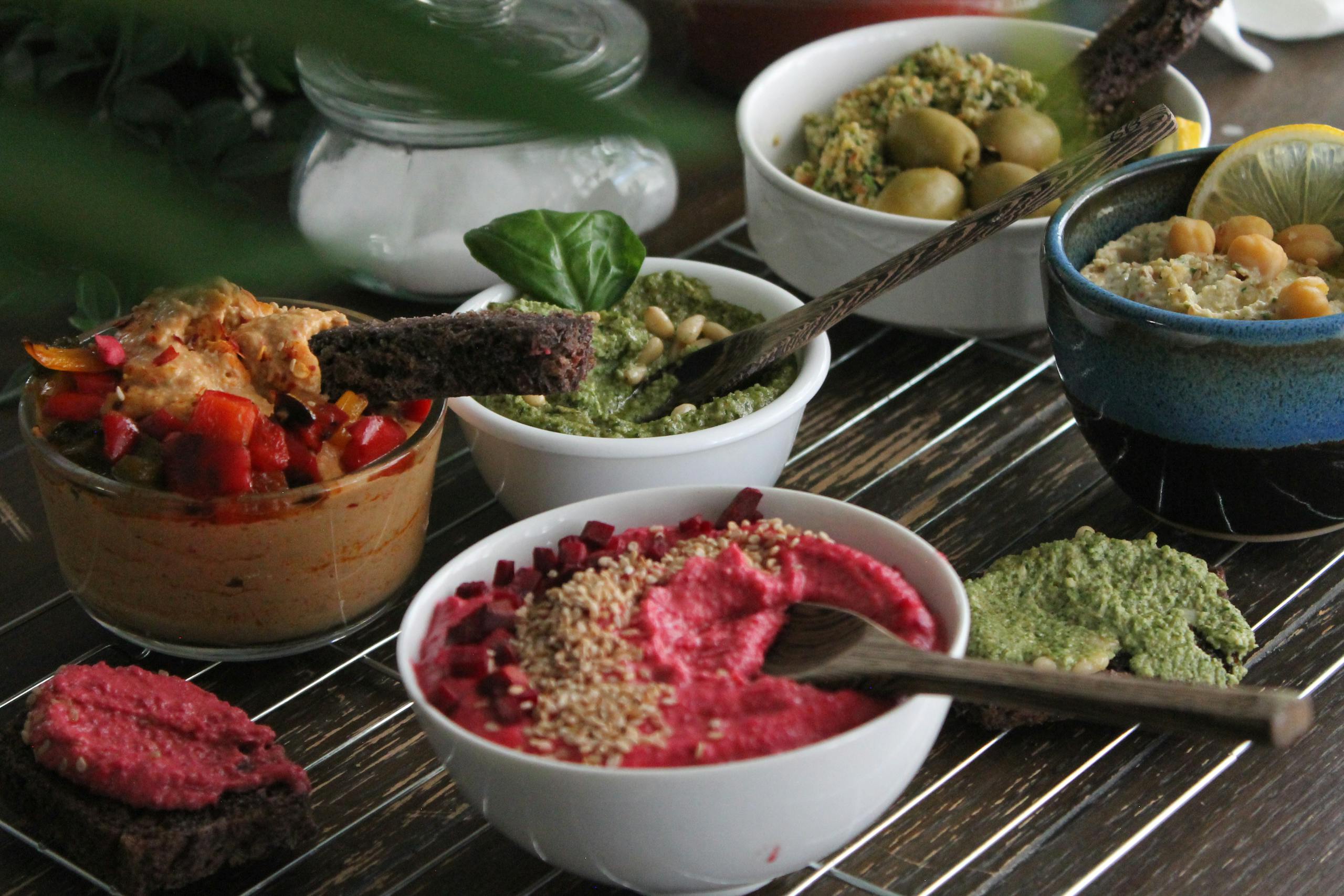 An enticing array of hummus varieties with toppings and colorful garnishes on a wooden table.