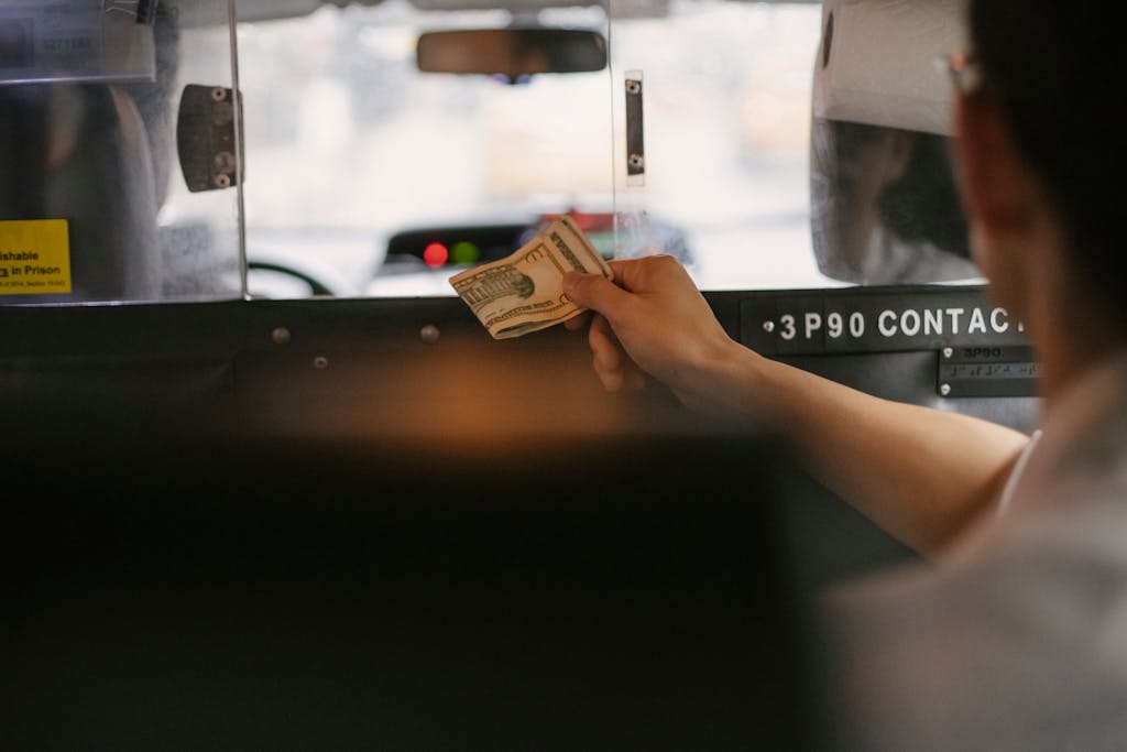 Back view of anonymous male passenger giving dollars to driver through window of contemporary taxi in megapolis