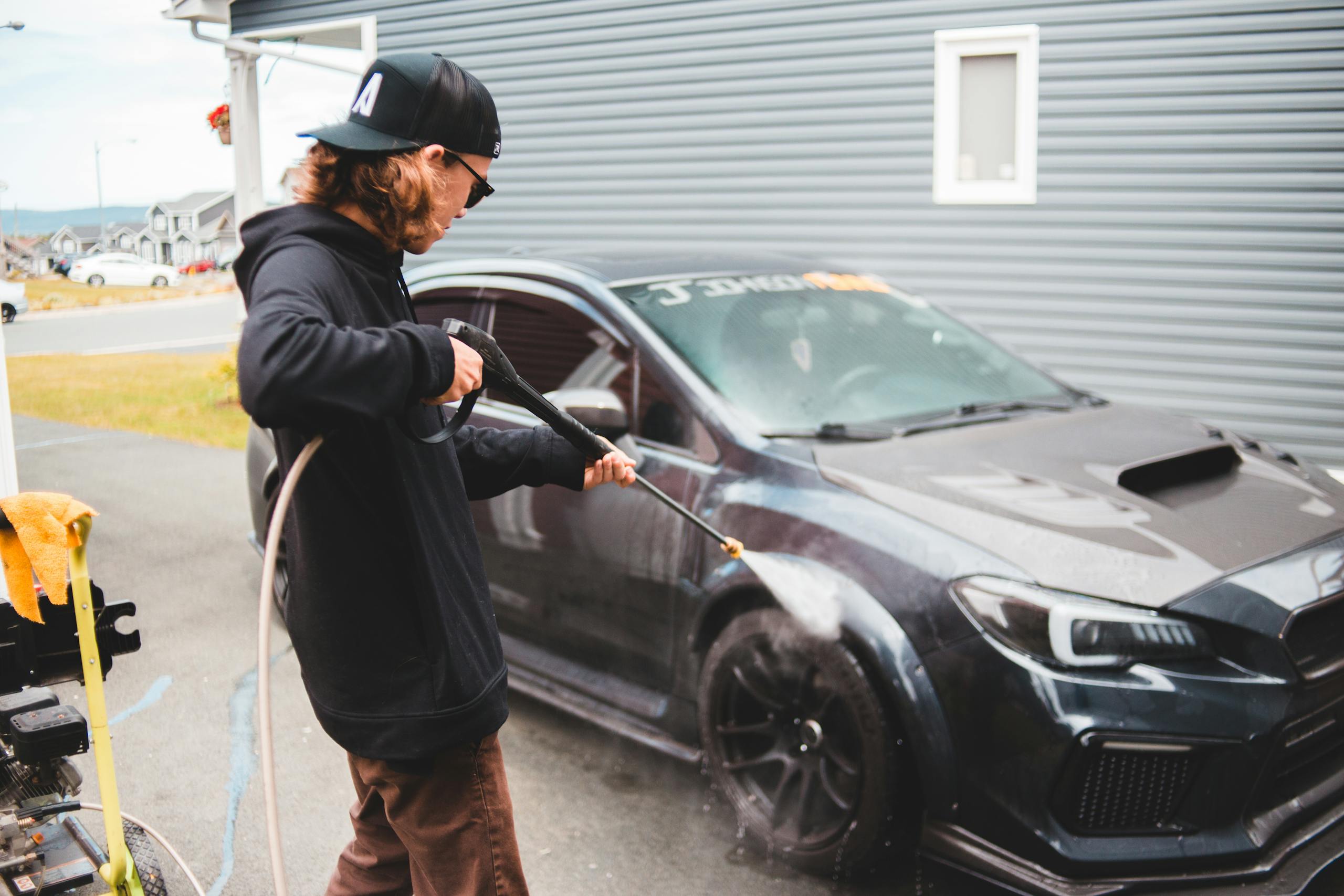 Back view of faceless worker using hosepipe while washing expensive black luxury sports car in daytime