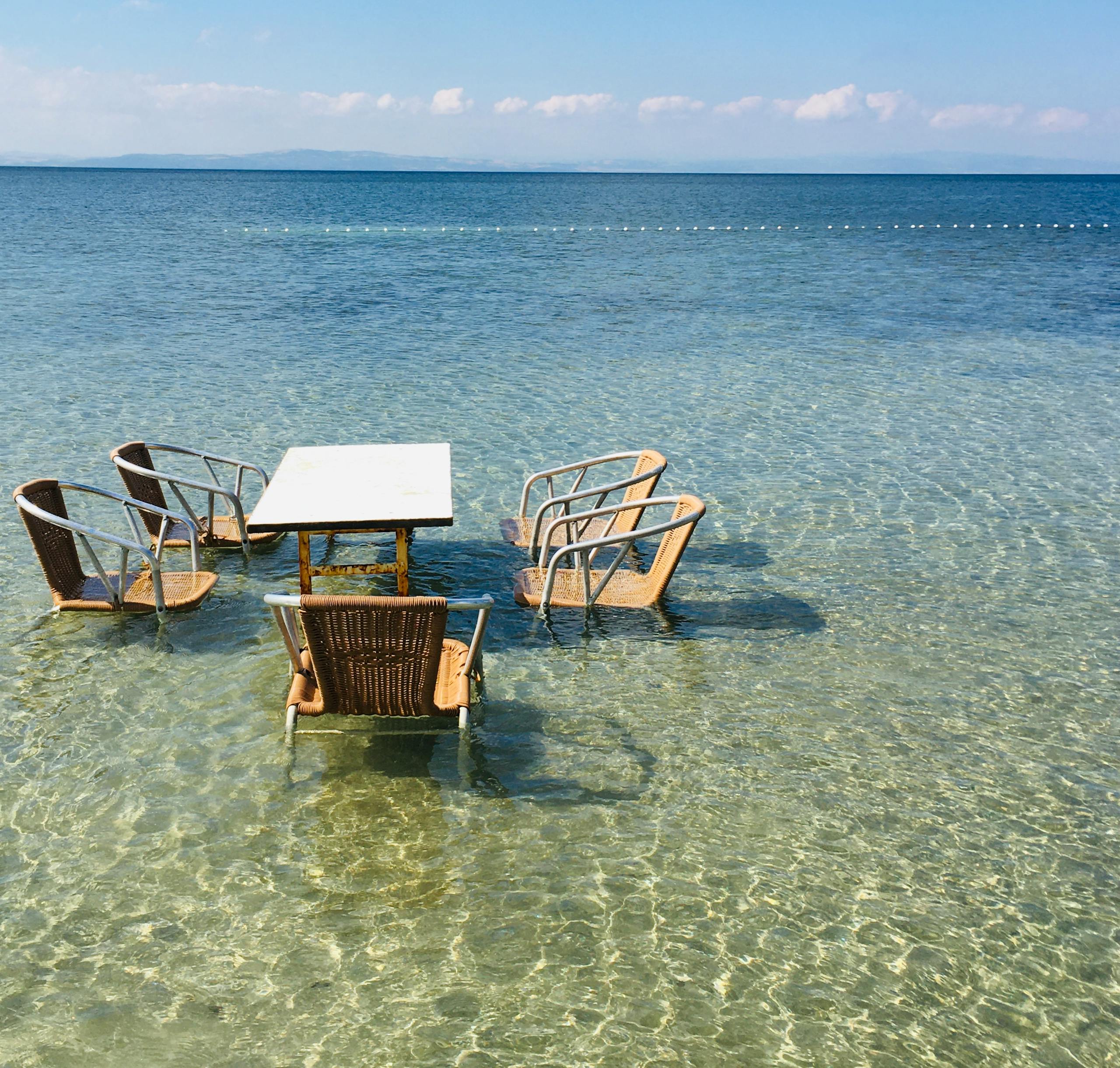 Chairs and table set in shallow crystal clear ocean water, Erdek, Türkiye.