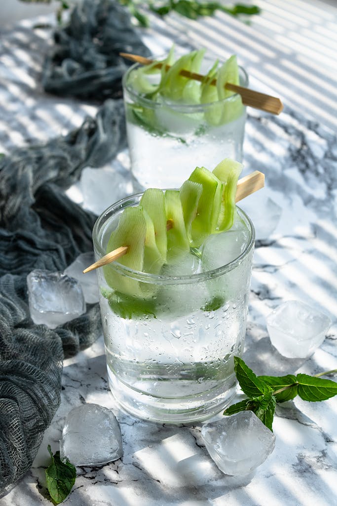 Chilled cucumber vodka cocktails with ice cubes and mint on a marble surface.