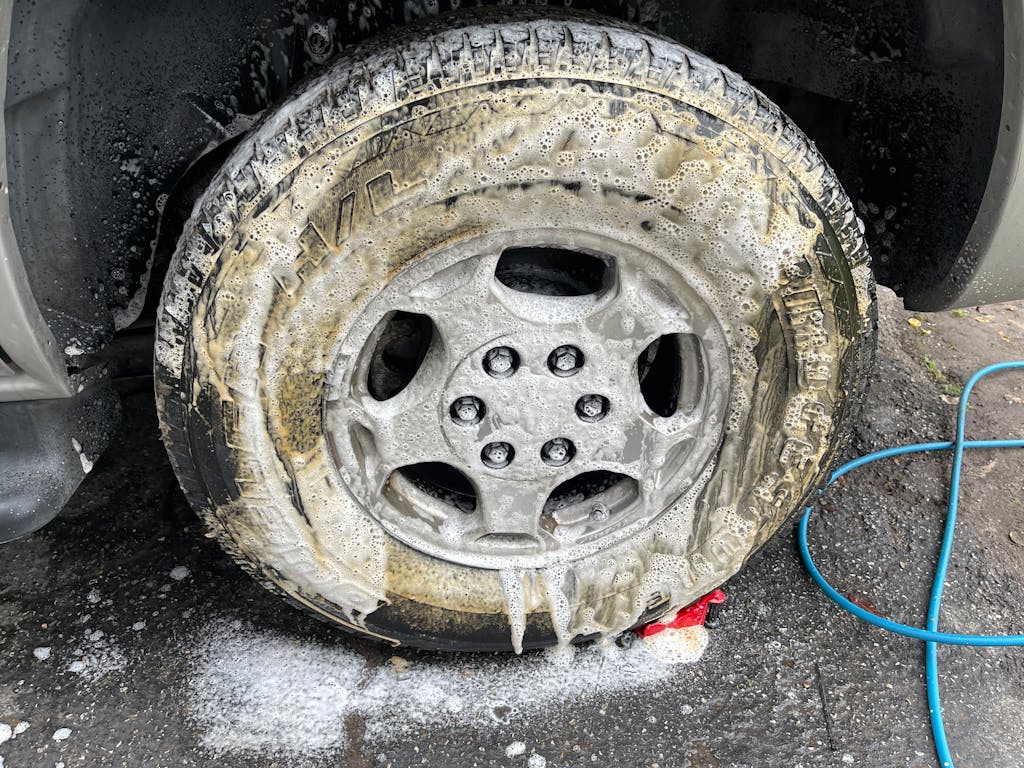 Close-up of a car wheel being cleaned with soap during a detailed car wash.