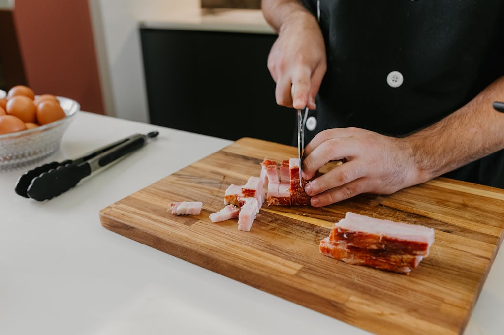 Close-up of a chef slicing bacon on a wooden board in the kitchen.