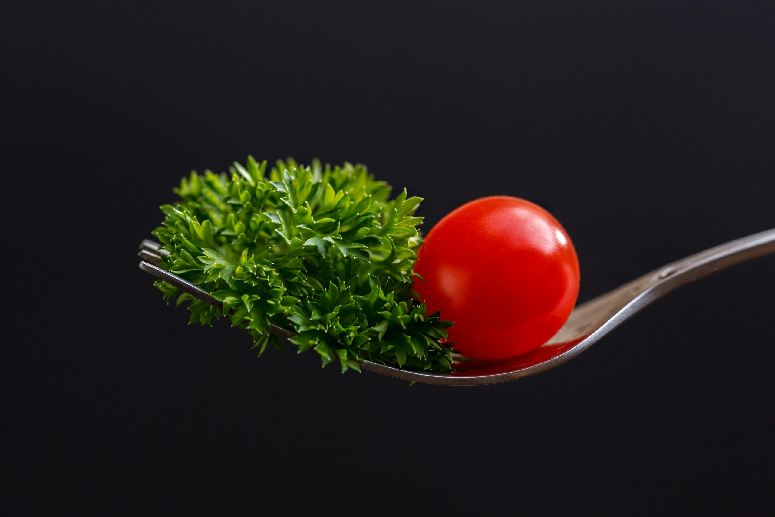 Close-up of a cherry tomato and parsley on a fork against a dark background.