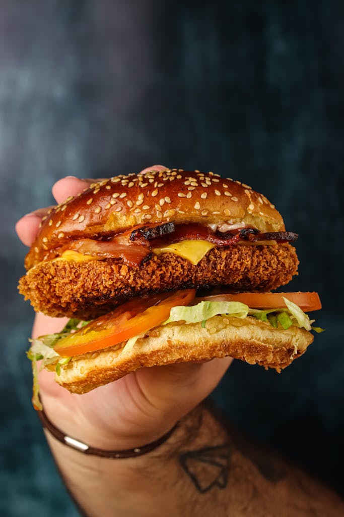 Close-up of a hand holding a delicious crispy chicken burger with fresh toppings.