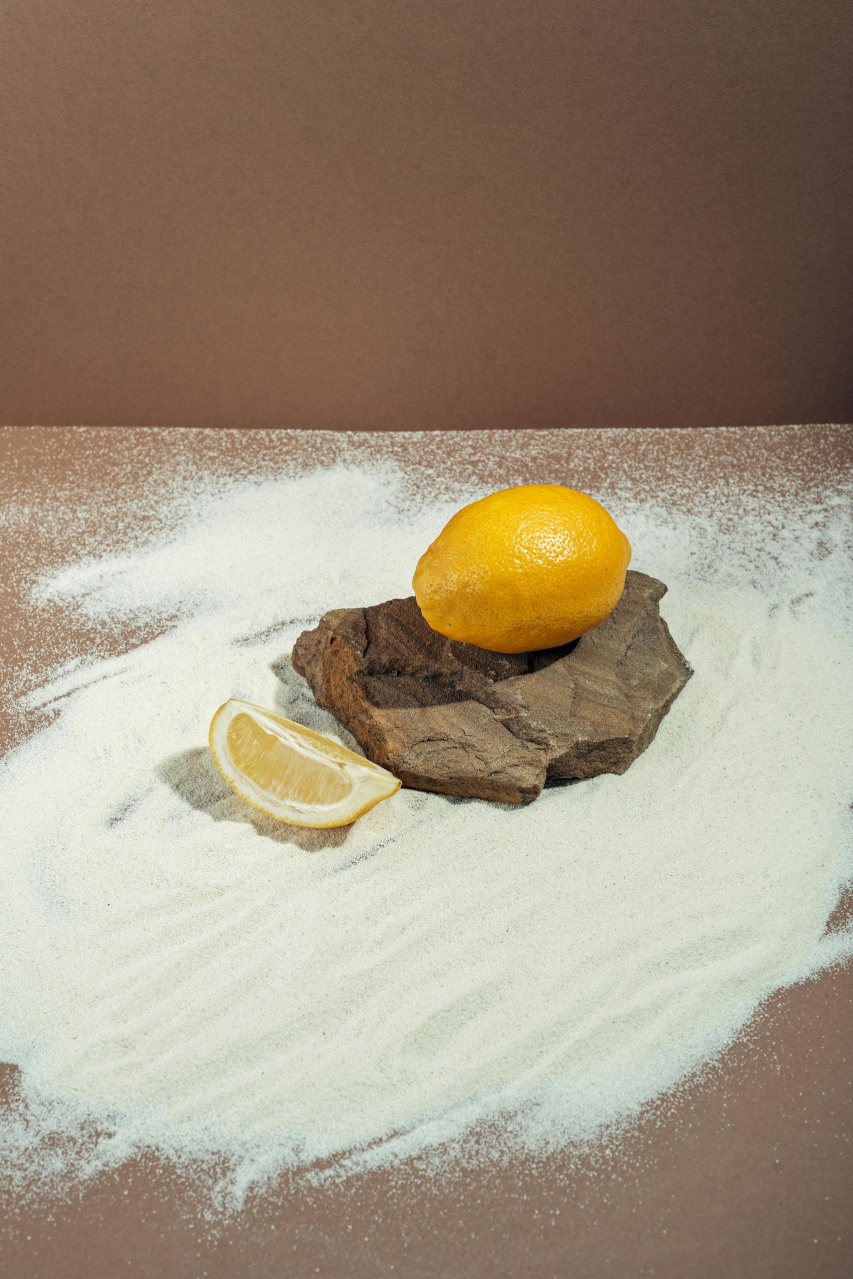 Close-up of a lemon and a slice on wood with a brown background and white sand.