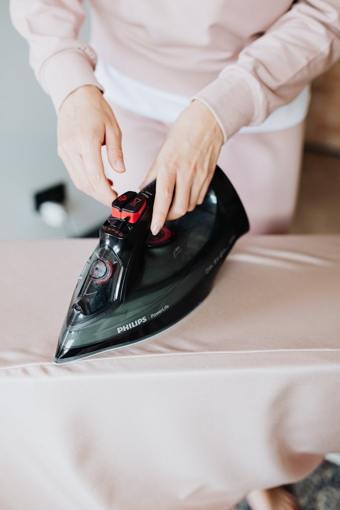 Close-up of a person using a Philips steam iron on a beige fabric indoors.