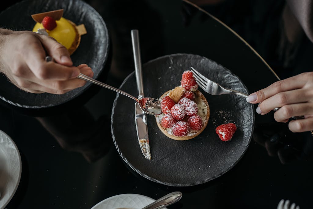 Close-up of a raspberry tart with powdered sugar on a black plate, top view.
