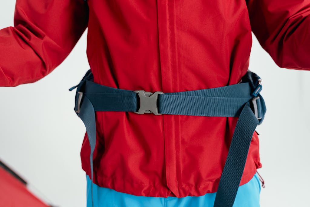 Close-up of a red jacket featuring a secured strap buckle, ideal for hiking gear.