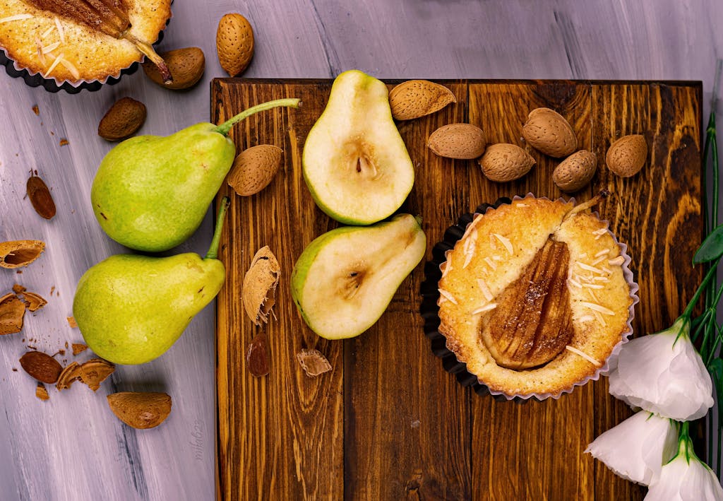 Close-up of a rustic pear tart surrounded by fresh pears and almonds on a wooden board.