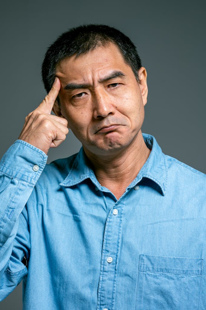 Close-up of an adult man pondering deeply, wearing a blue denim shirt.