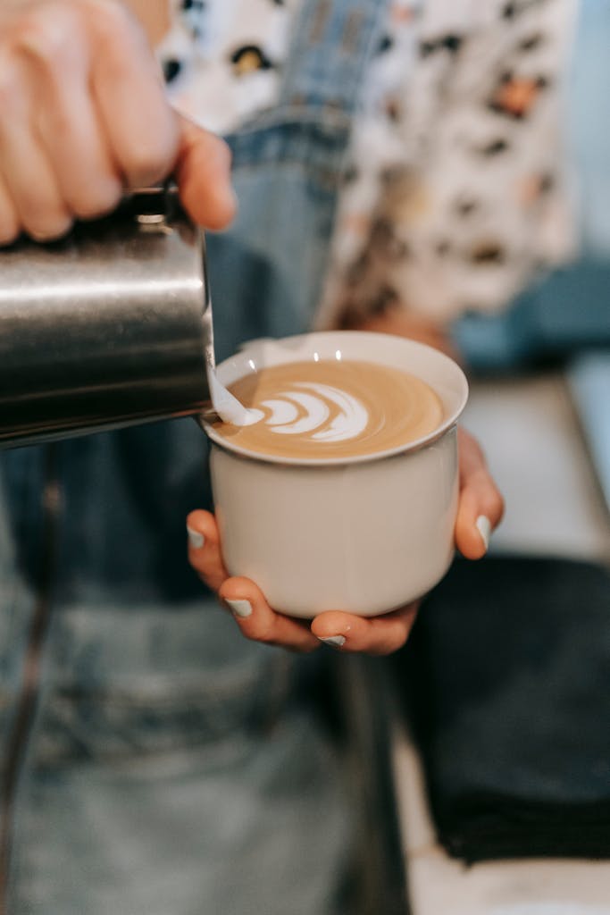 Close-up of barista pouring milk to create latte art in a cozy coffee shop.