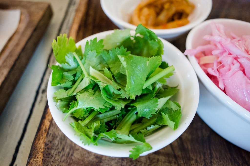 Close-up of fresh cilantro leaves and pickled vegetables in bowls, emphasizing healthy ingredients.