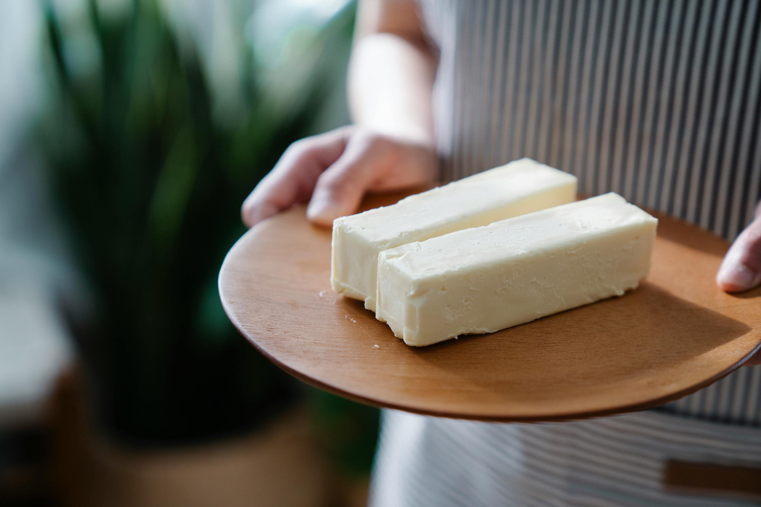 Close-up of hands holding a wooden plate with two sticks of butter.