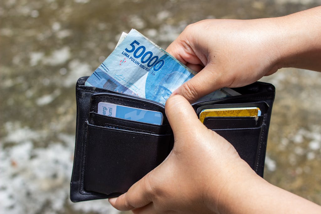 Close-up of hands inserting Indonesian Rupiah into wallet outdoors.