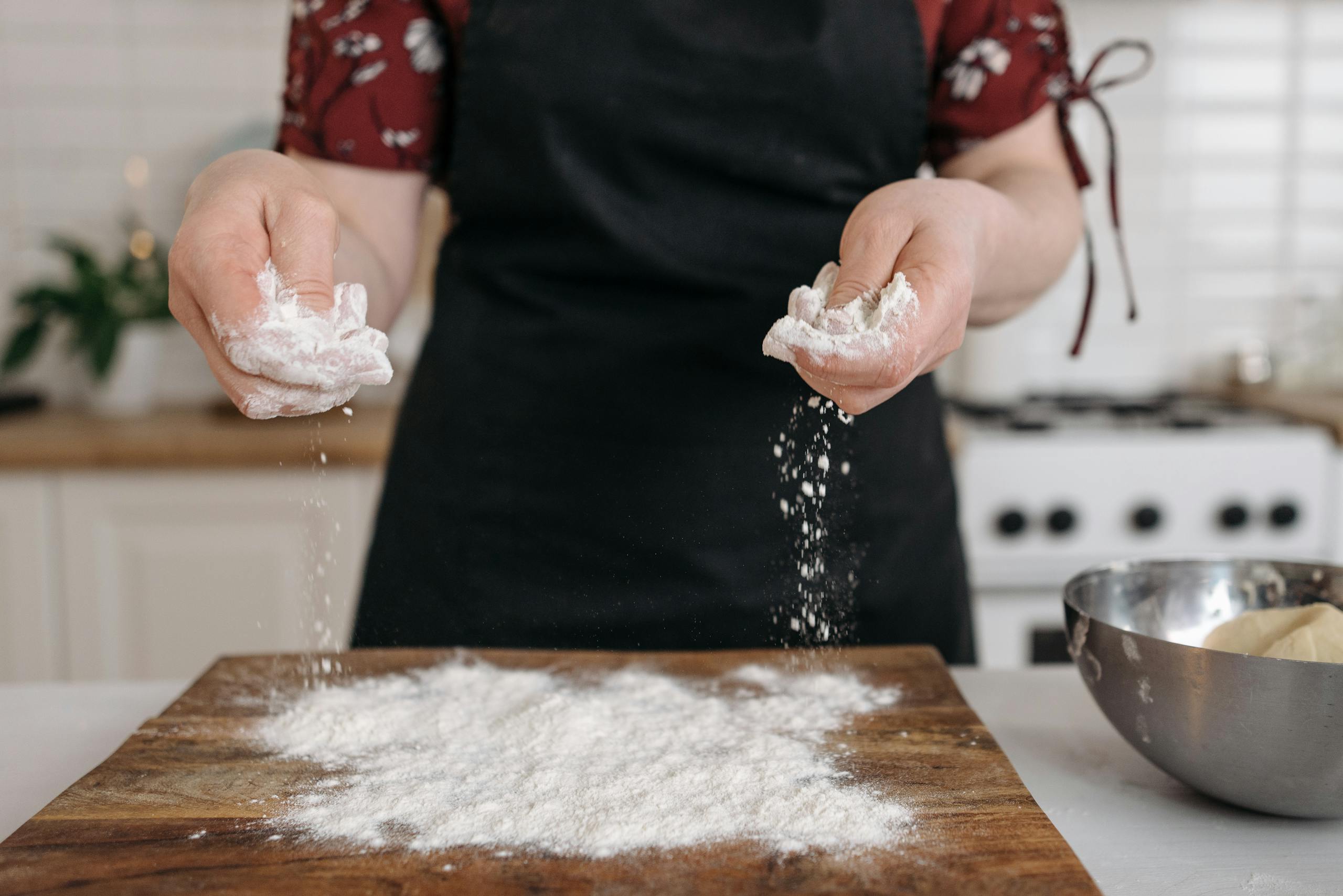 Close-up of hands sprinkling flour on a chopping board, ideal for food preparation themes.