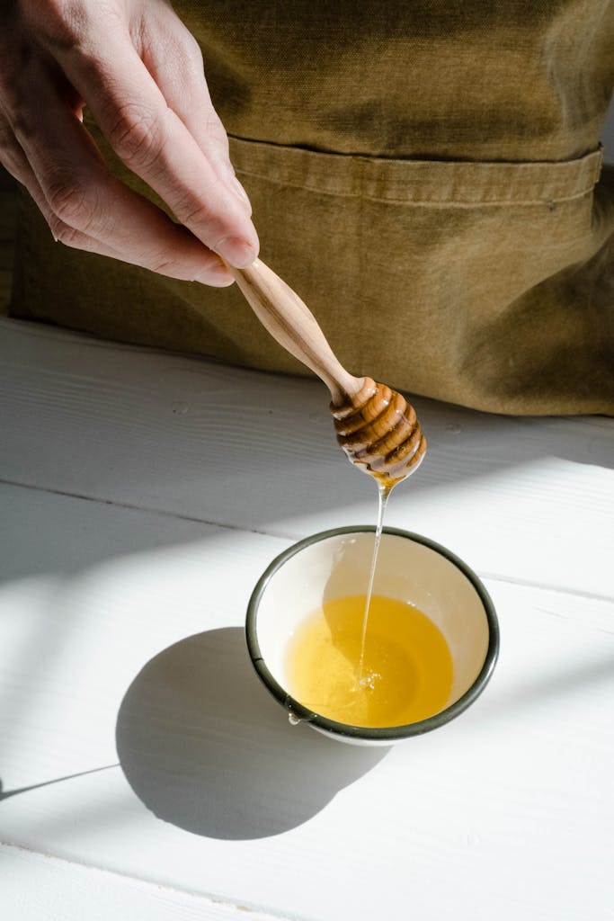 Close-up of honey being poured into a bowl using a wooden honey dipper, casting a shadow.