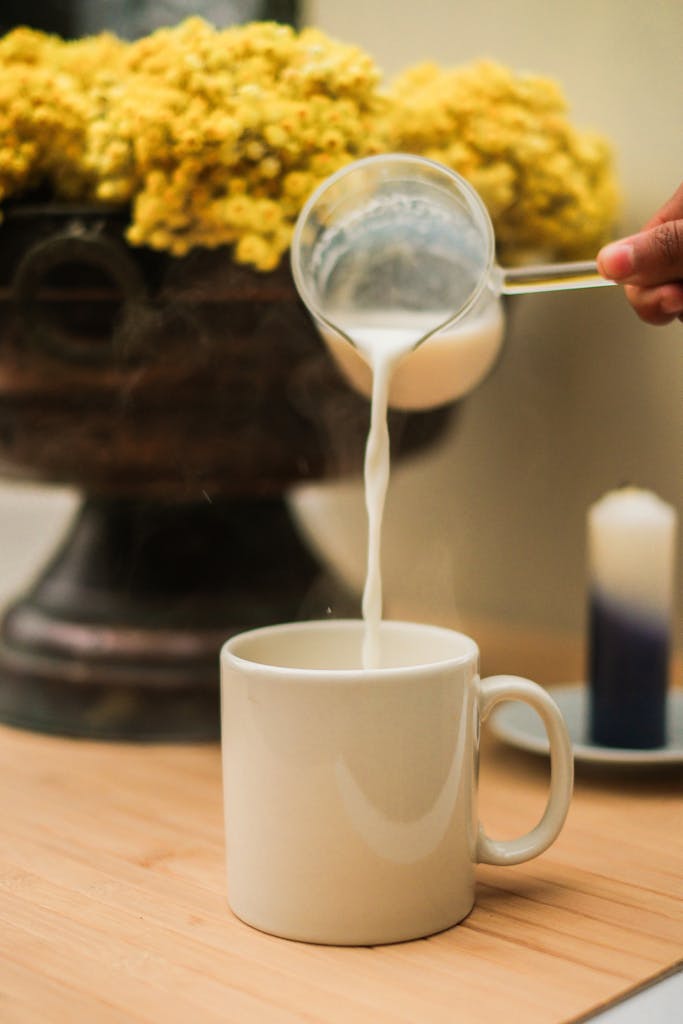 Close-up of milk being poured into a cup with a floral background, ideal for lifestyle concepts.