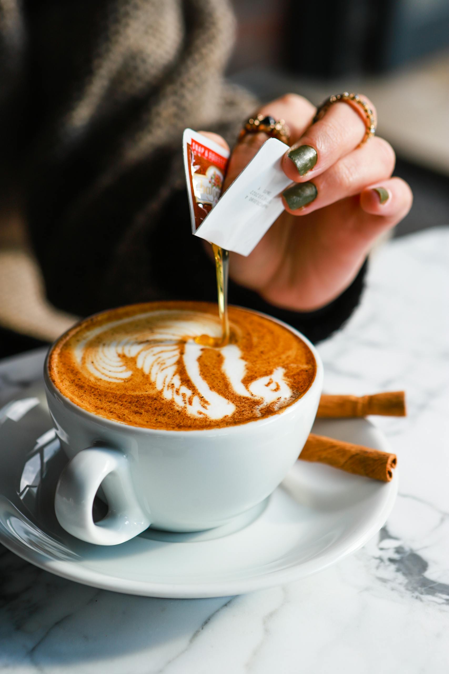 Close-up of syrup being poured into a cappuccino with latte art on a marble table.