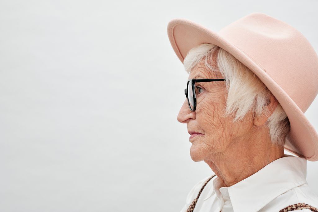 Close-up side view of a senior woman wearing eyeglasses and a stylish hat, showcasing elegance and wisdom.