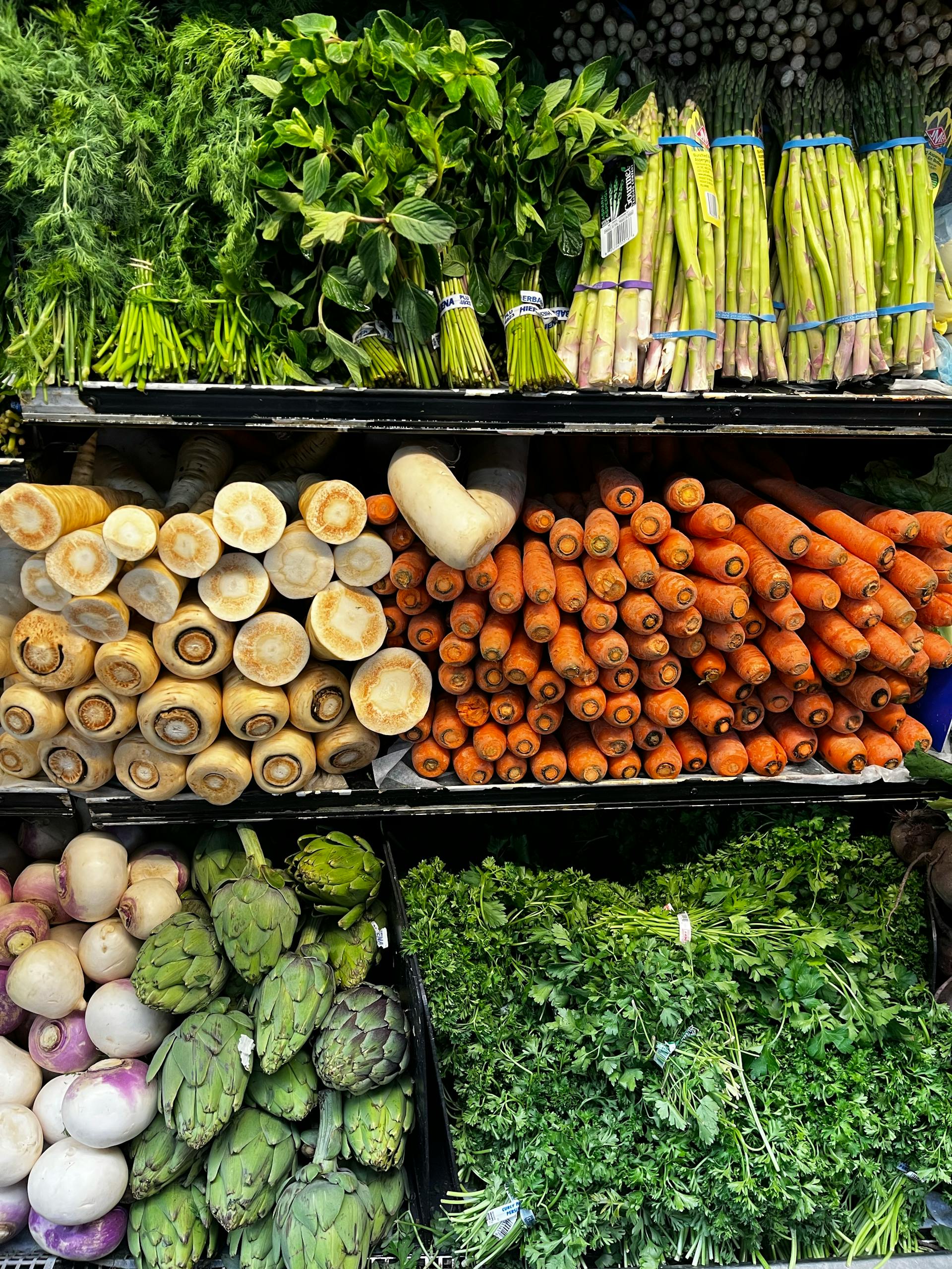 Colorful assortment of fresh vegetables including asparagus, carrots, and herbs in a grocery store display.