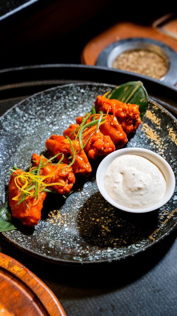 Crispy buffalo wings with creamy dip served on a stylish plate.