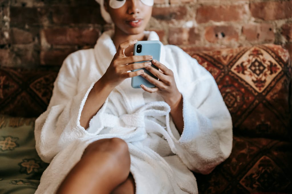 Crop anonymous ethnic female with eye patches chatting on mobile phone while sitting with crossed legs on couch in house